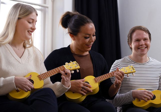 kolme iloista aikuista soittaa ukuleleja